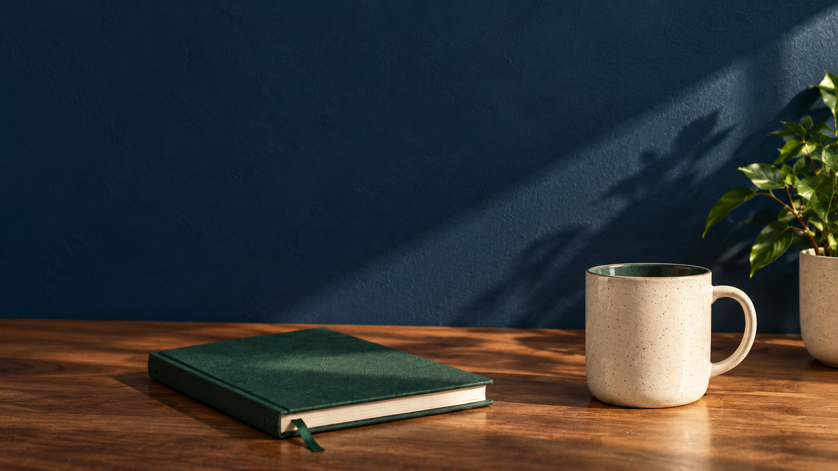 A green notebook, coffee mug, and plant in a quiet studio